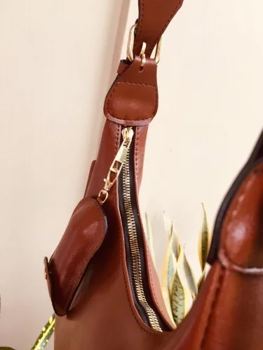 Tas cokelat tergantung dengan ritsleting logam emas di sisi atas dan pouch mini cokelat yang tergantung di pangkal tali