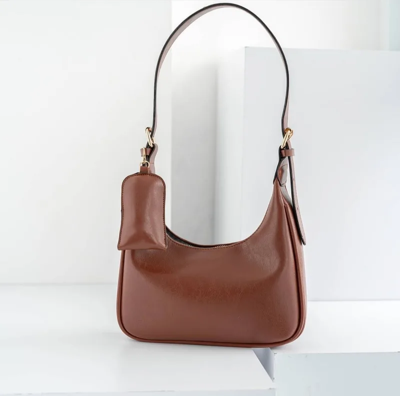 Tas hobo cokelat kemerahan dengan tali bahu dan pouch kecil yang dikaitkan di tali, dipajang di atas balok putih