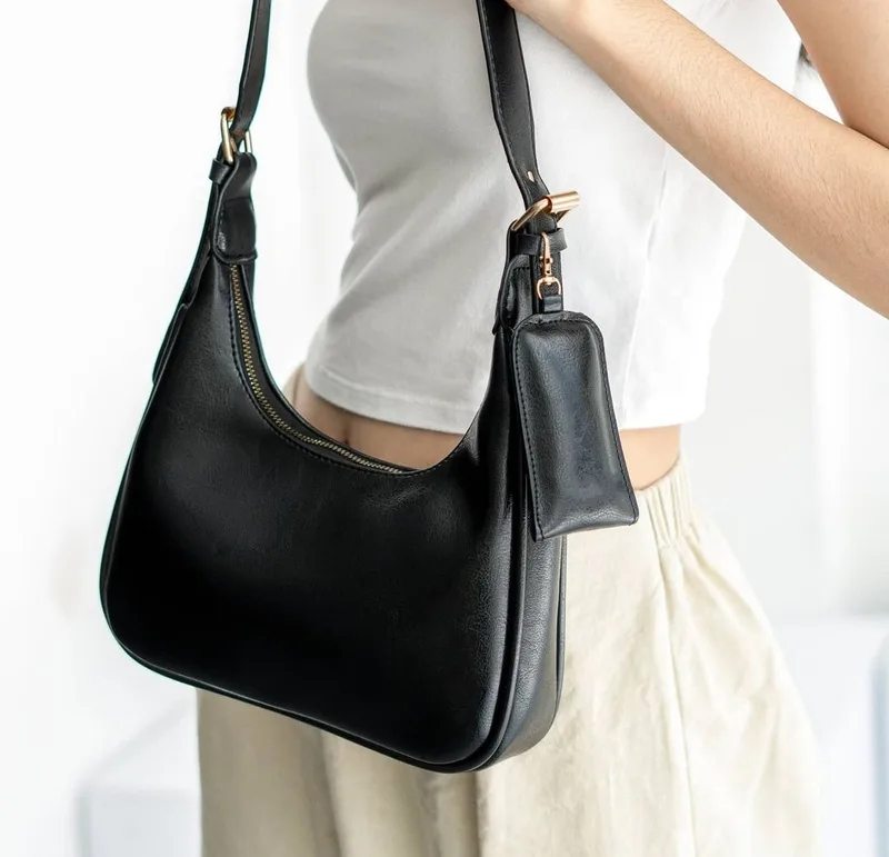 Perempuan berkaus putih menyandang tas hobo hitam di bahu, dengan pouch kecil hitam tergantung di tali tas