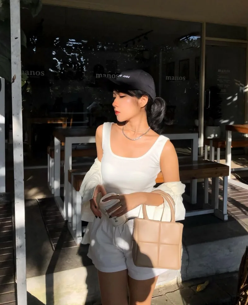 Perempuan bertopi hitam dengan atasan putih menjinjing tas berpanel kotak warna cokelat muda di depan sebuah kafe