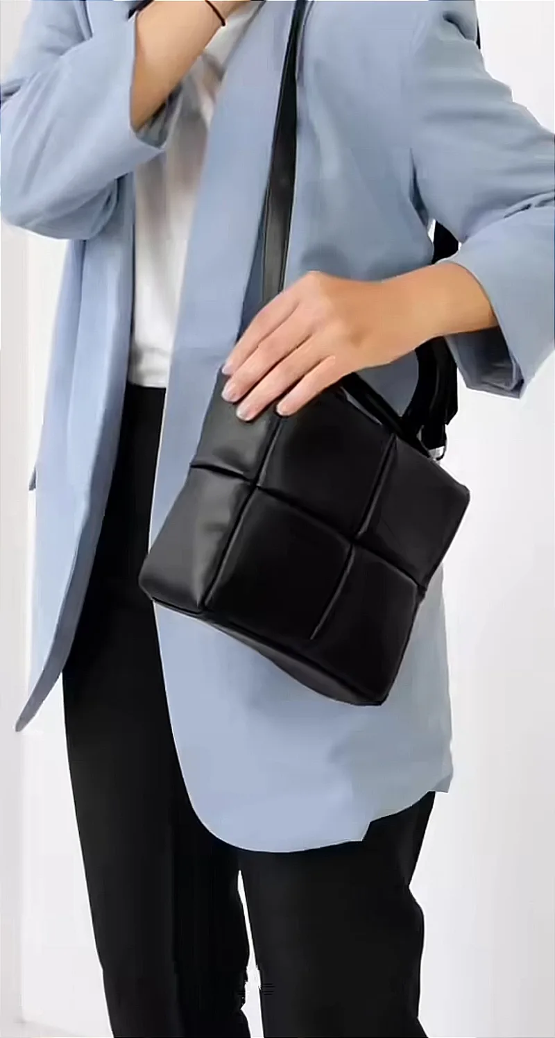 Orang berblazer biru muda dan celana hitam menyandang tas berpanel kotak warna hitam di bahu dengan tali panjang hitam