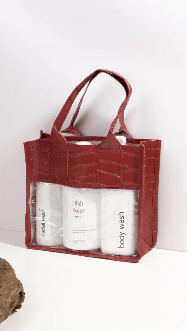 Tas jinjing bertekstur croco warna merah dengan panel depan transparan yang memperlihatkan tiga botol sabun dan sampo di dalamnya