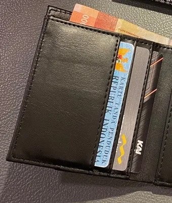 Bagian dalam dompet lipat Bova berwarna hitam dengan KTP dan satu kartu lain terselip di slot kartu bertingkat, serta uang kertas di kantong belakang
