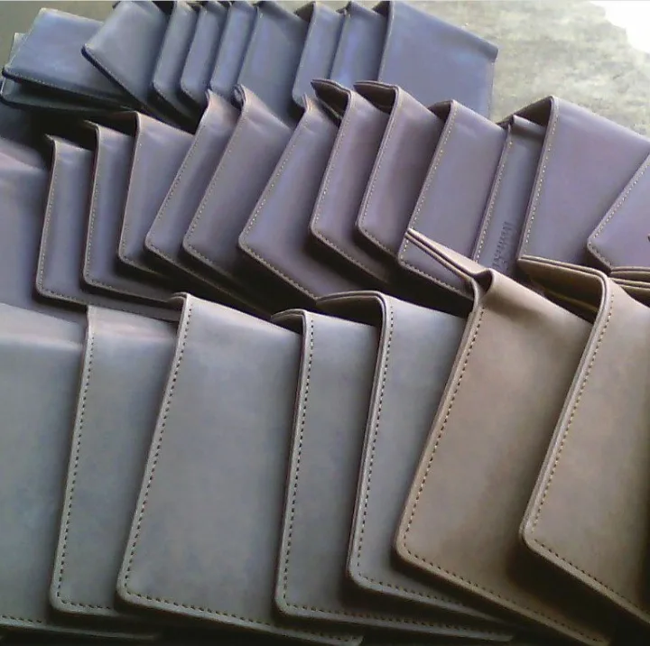Deretan dompet lipat warna abu-abu keunguan dan cokelat keabuan tersusun miring berlapis di atas meja