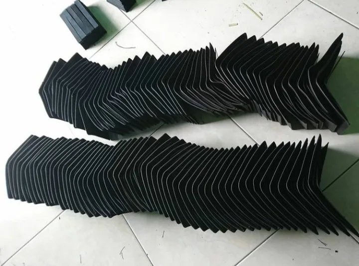 Ratusan potongan bahan hitam disusun berjajar bertumpuk membentuk dua barisan panjang di atas lantai keramik putih