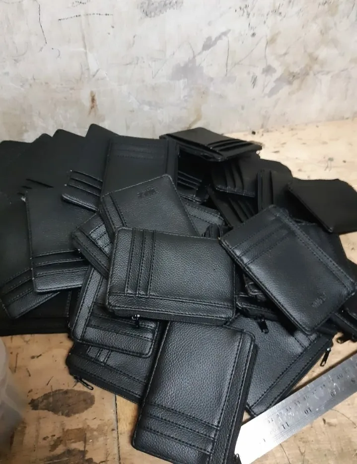 Dompet dan card holder hitam bertumpuk di meja kerja kayu di samping penggaris besi