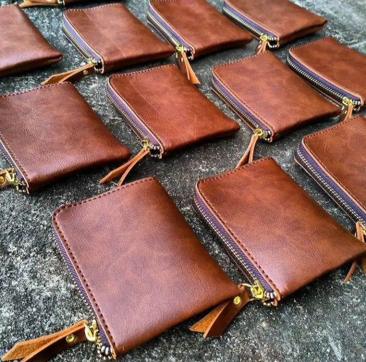 Dompet ritsleting warna cokelat tua dengan penarik ritsleting berumbai, berjajar di atas permukaan batu