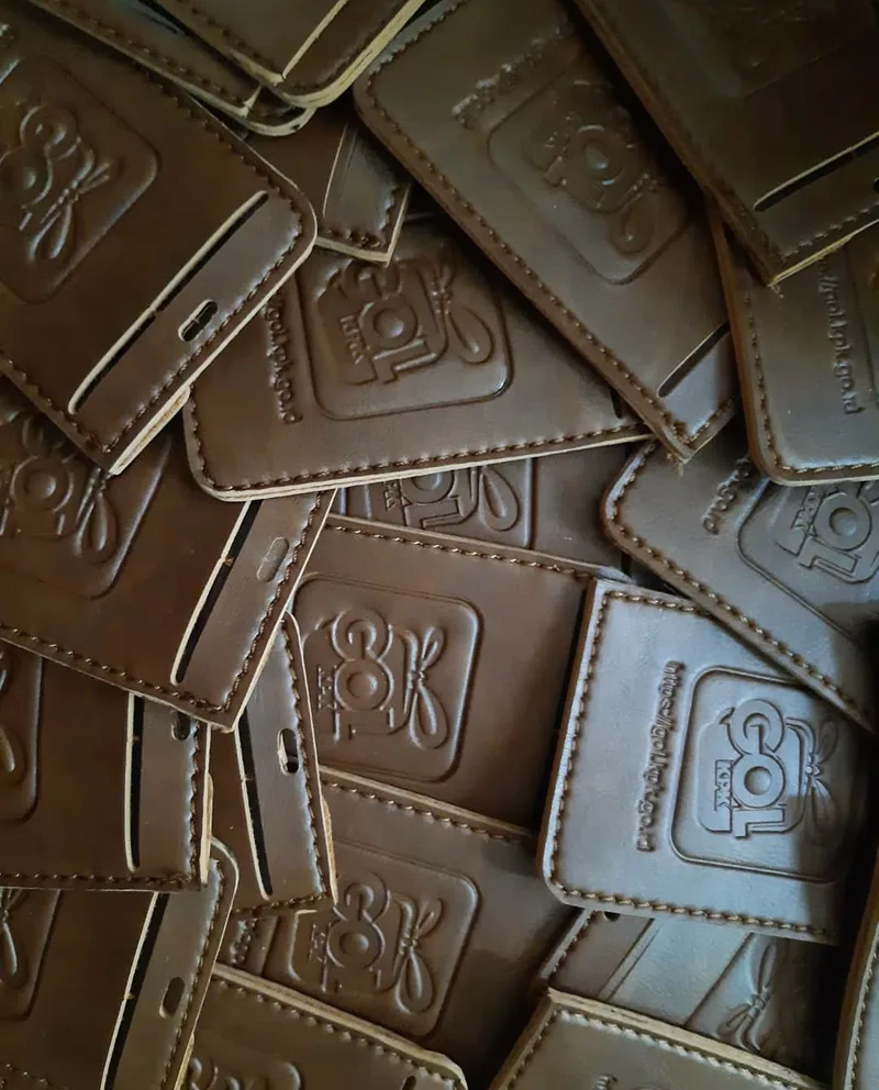 Potongan kulit cokelat tua dengan logo timbul hasil emboss dan jahitan tepi berwarna krem