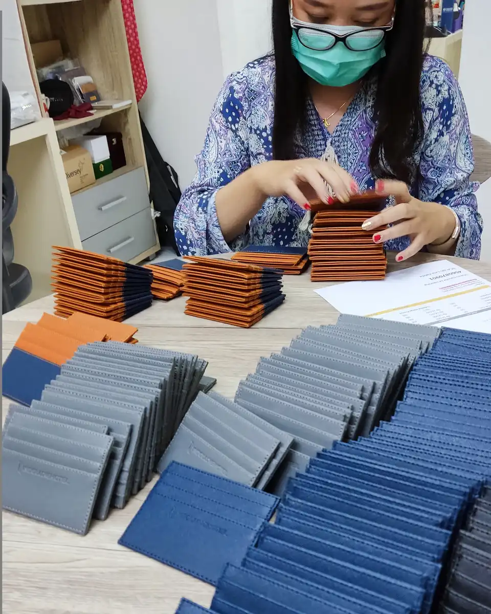 Perempuan bermasker menyusun tumpukan card holder oranye, abu-abu, dan biru di atas meja kerja